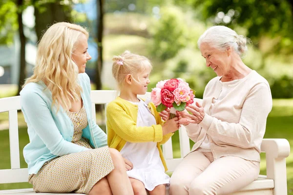 Glückliche Familie schenkt Oma Blumen im Park — Stockfoto