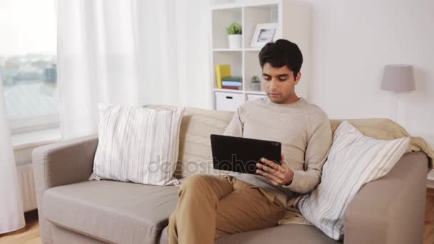 Hombre con tablet pc sentado en el sofá en casa — Vídeos de Stock