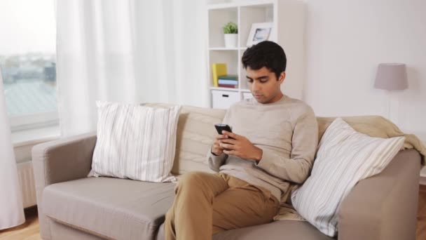 Homem com smartphone sentado no sofá em casa — Vídeo de Stock