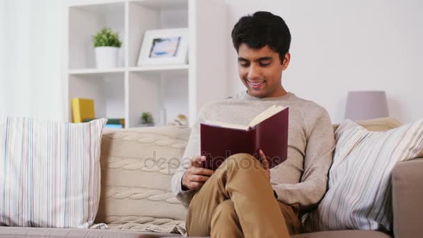 Hombre sentado en el sofá y leyendo libro en casa — Vídeos de Stock