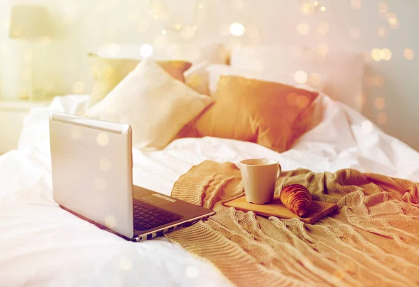 Laptop, coffee and croissant on bed at cozy home — Stock Photo, Image