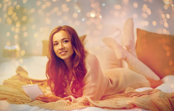 Glückliche junge Frau mit Notizbuch zu Hause im Bett — Stockfoto