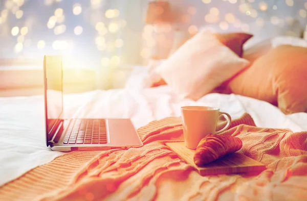 Laptop, coffee and croissant on bed at cozy home — Stock Photo, Image