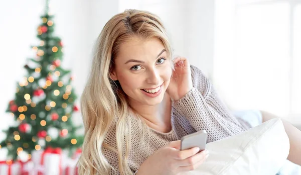 Mujer feliz con teléfono inteligente en la cama en Navidad — Foto de Stock