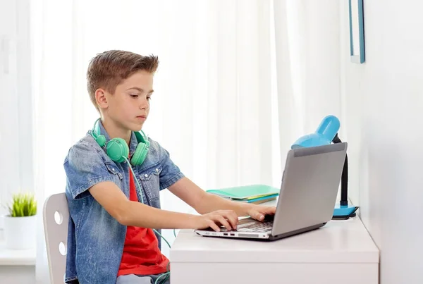 Menino com fones de ouvido digitando no laptop em casa — Fotografia de Stock