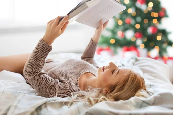 Giovane donna che legge libro a letto a Natale — Foto Stock