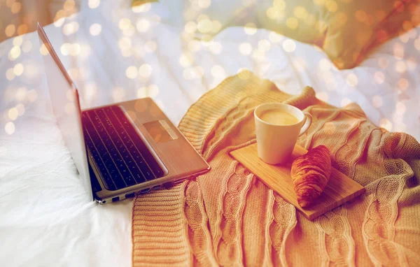 Ordinateur portable, café et croissant au lit à la maison confortable — Photo