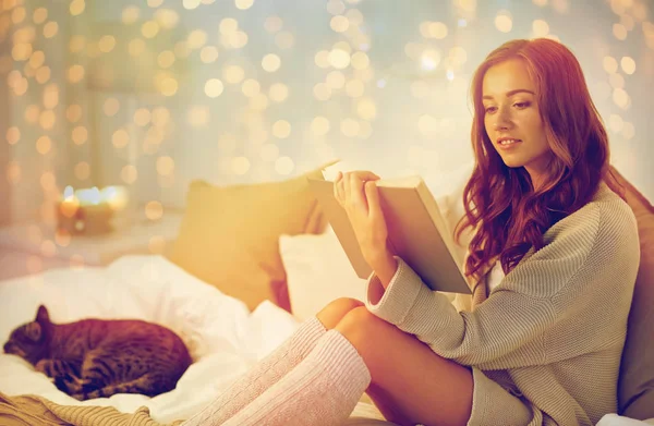Happy young woman reading book in bed at home — Stock Photo, Image