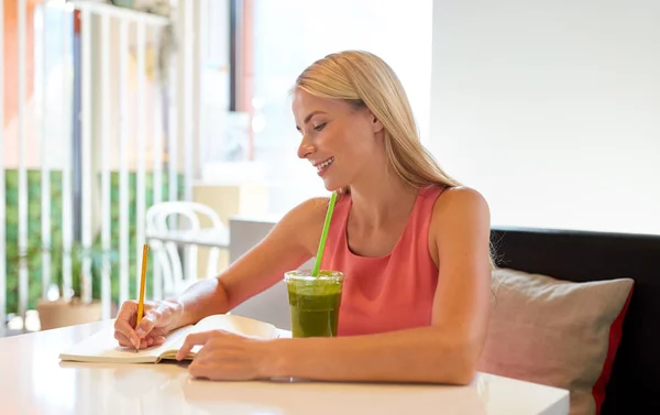 Frau mit Getränk schreibt an Notizbuch im Restaurant — Stockfoto