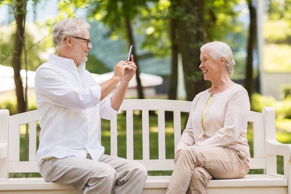 old woman photographing man by smartphone in park