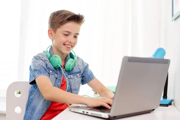 Niño feliz con auriculares escribiendo en el ordenador portátil en casa —  Fotos de Stock