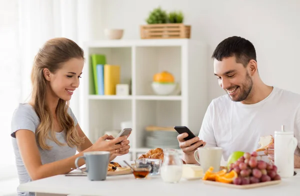 Пара со смартфонами, завтракающими дома — стоковое фото