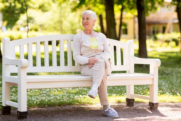 Lycklig senior kvinna sitter på bänken på sommaren park — Stockfoto