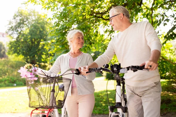 Счастливая пожилая пара с велосипедами в летнем парке — стоковое фото