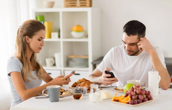 Casal com smartphones tomando café da manhã em casa — Fotografia de Stock
