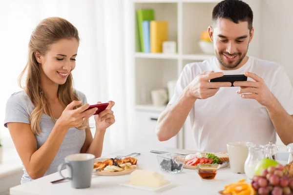 Пара со смартфонами, завтракающими дома — стоковое фото