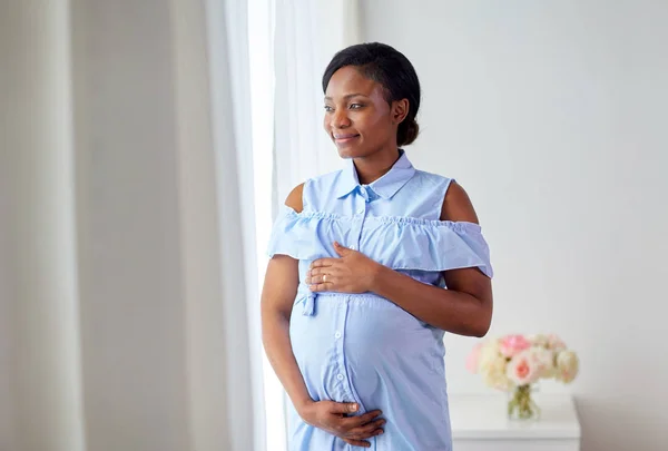 Pregnant woman looking through window at home — Stock Photo, Image