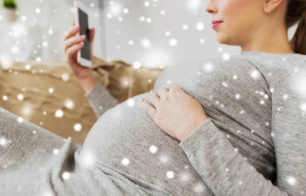 Счастливая беременная женщина со смартфоном дома — стоковое фото