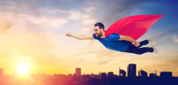 Hombre feliz en capa de superhéroe rojo volando sobre la ciudad — Foto de Stock