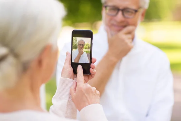 Стара жінка фотографує чоловіка за допомогою смартфона в парку — стокове фото