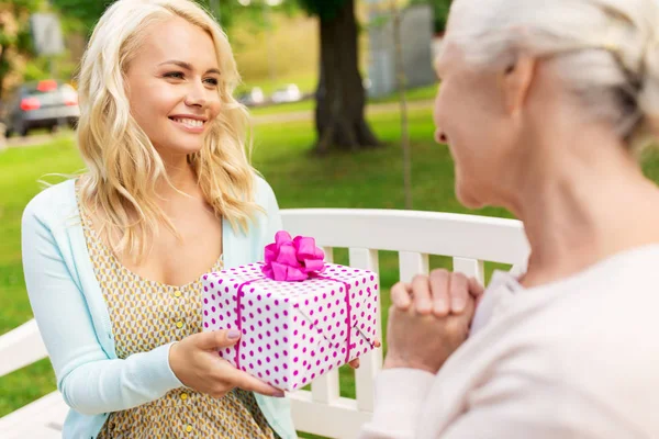Daughter giving present to senior mother at park — Stock Photo, Image