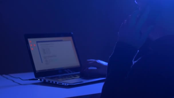 Хакер с программой на ноутбуке, звонящий на сотовый — стоковое видео