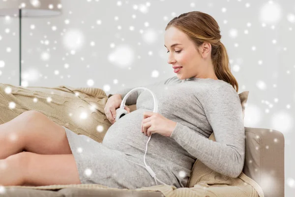 Zwangere vrouw met hoofdtelefoon op haar buik — Stockfoto