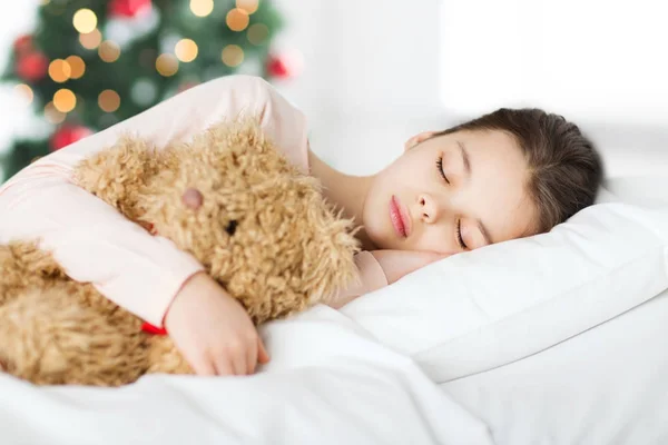 Chica durmiendo con osito de peluche en la cama en Navidad — Foto de Stock