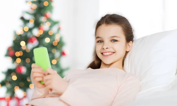快乐的女孩在床上与智能手机在圣诞节 — 图库照片
