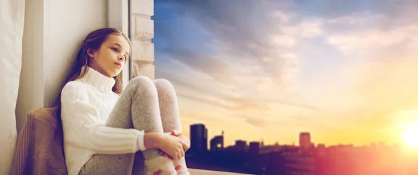 Sad girl sitting on sill at home window — Stock Photo, Image