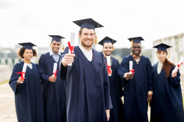 Glada studenter i murbruk styrelser med diplom — Stockfoto