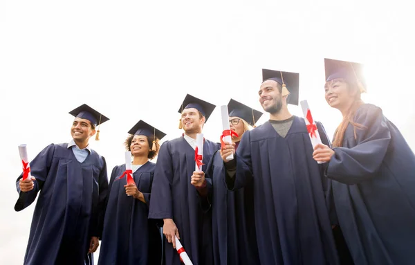 Happy students in mortar boards with diplomas — Stock Photo, Image