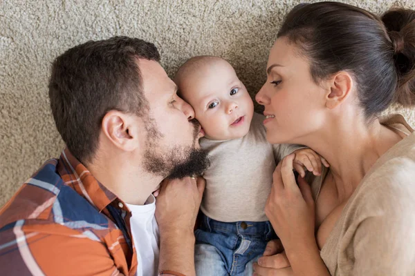 Happy family lying on floor and kissing their baby — Stock Photo, Image