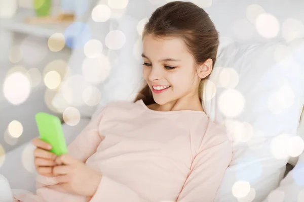 Glückliches Mädchen im Bett mit Smartphone über Licht — Stockfoto