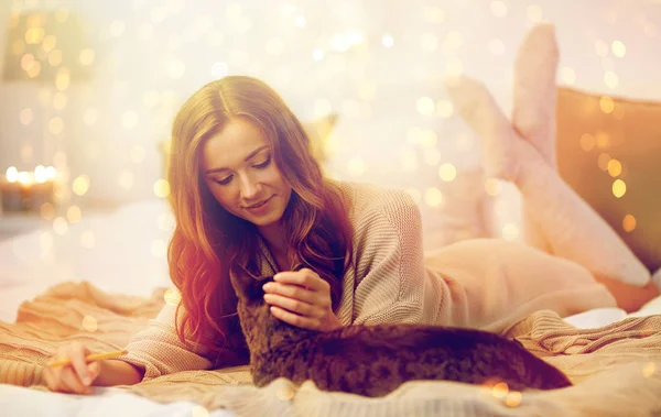 Счастливая молодая женщина с кошкой, лежащей в постели дома — стоковое фото