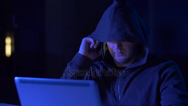 Hacker with laptop calling on cellphone — Stock Video