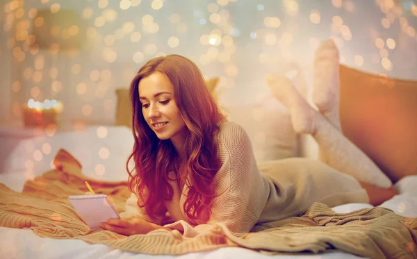 Glad ung kvinna med anteckningsboken i sängen hemma — Stockfoto
