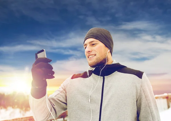 Šťastný muž s sluchátka a smartphone v zimě — Stock fotografie
