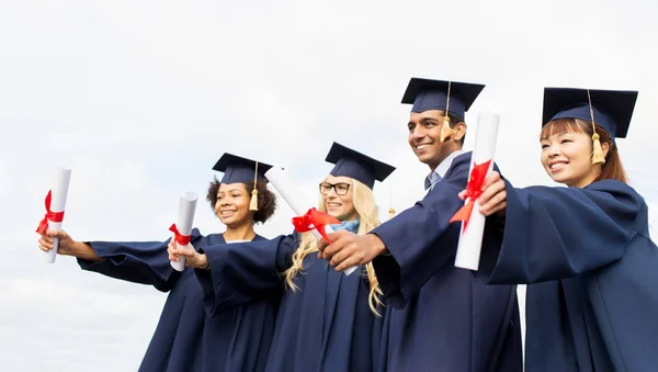 Happy students in mortar boards with diplomas — Stock Photo, Image