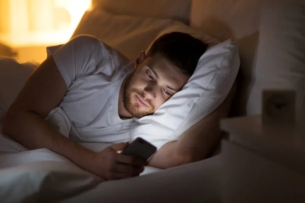 Jovem feliz com smartphone na cama à noite — Fotografia de Stock