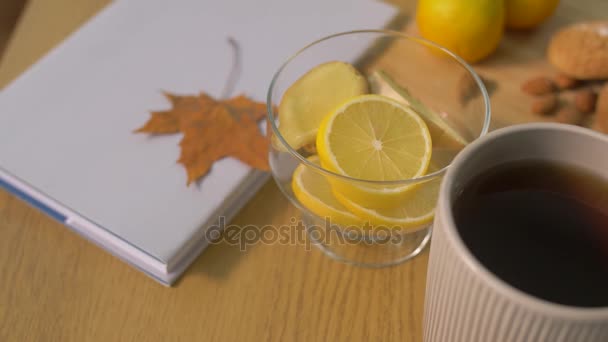 Kniha, citron, šálek čaje, oříšky a soubory cookie na stole — Stock video