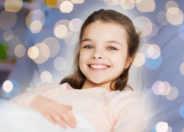 Happy smiling girl lying awake in bed over lights — Stock Photo, Image