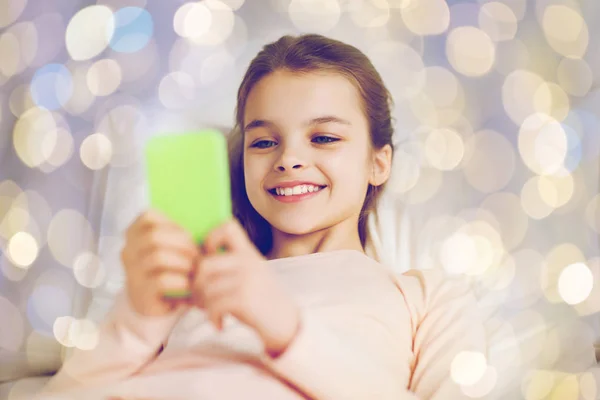 Glückliches Mädchen im Bett mit Smartphone über Licht — Stockfoto