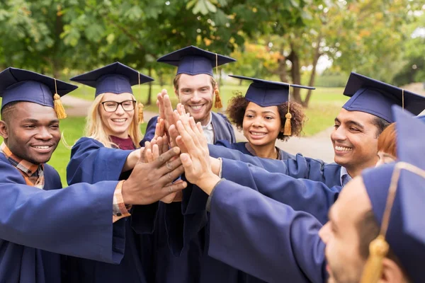 Estudantes felizes em placas de argamassa fazendo alta cinco — Fotografia de Stock