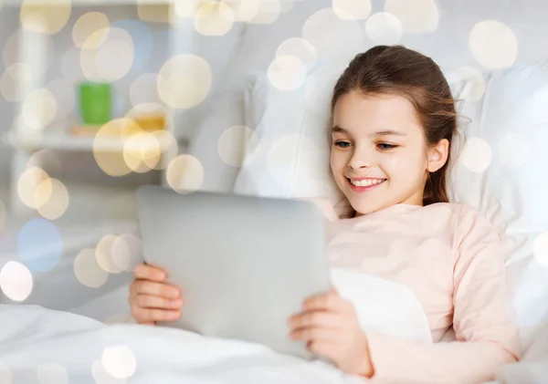 Chica feliz en la cama con la tableta de PC sobre las luces —  Fotos de Stock