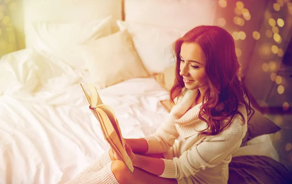 Happy young woman reading book in bed at home — Stock Photo, Image