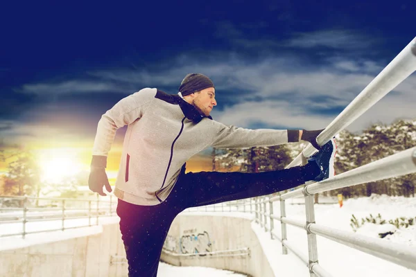 Sportovní muž strečink nohou na plot v zimě — Stock fotografie