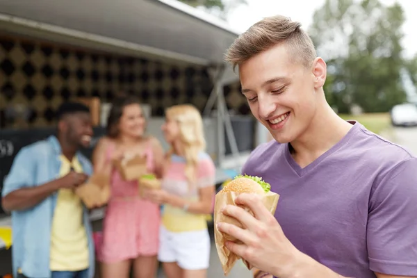 Hombre feliz con hamburguesa y amigos en camión de comida — Foto de Stock