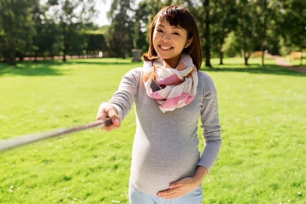 Glad gravid asiatisk kvinna tar selfie på park — Stockfoto