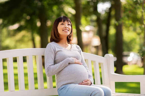 快乐怀孕的亚裔妇女坐在公园长凳上 — 图库照片